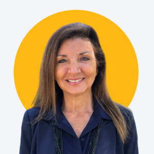 Photo of our CEO, Monica DeShazo. She has a yellow circle around her head and she is wearing a blue blouse with black beaded necklace.